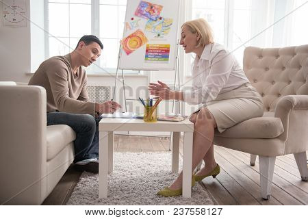 Art And Psychotherapy. Focused Man Visiting Jovial Psychologist While Trying Art Therapy