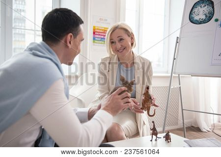 Psychological Parallel. Man Holding Toy While Communicating With Jolly Mature Psychologist