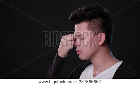 A Young Man Immitating A Headache Against A Black Background. Close-up Shot