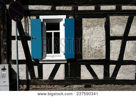 An Old Rickety Half-timbered House With A Striking Beam Construction And Shutters By The Window.