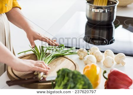 Cropped Image Of Woman Putting Green Onion On Cutting Board At Kitchen