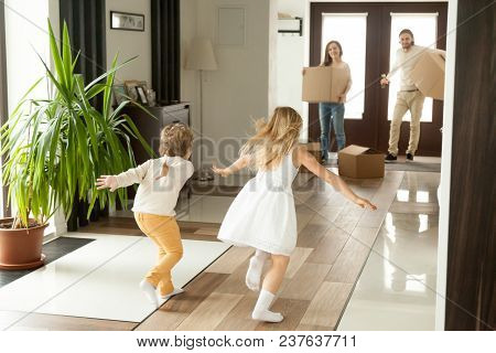 Rear View At Kids Running To Parents Holding Boxes On Moving Day Or After Shopping, Excited Happy Ch