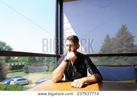 Thoughtful Caucasian Businessman Sitting On Sofa At Office, Wearing Black Shirt And Watch. Concept O