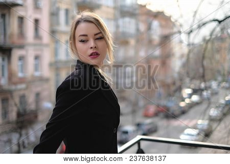 Portrait Of A Young Woman In A Black Suit Close-up Against A Background Of A Blurry City In The Rays