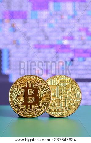 Two Gold Bitcoins Lie On The Green Surface On The Background Of The Display, Which Shows The Process