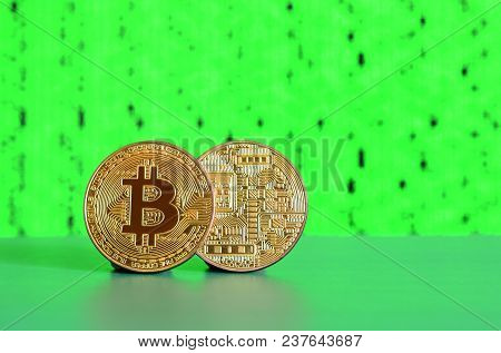 Two Gold Bitcoins Lie On The Green Surface On The Background Of The Display, Which Shows The Process