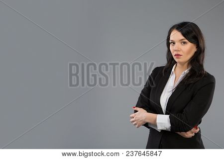 Standing Businesswoman Portrait On Grey Background And Looking At Camera. Copy Space At Left