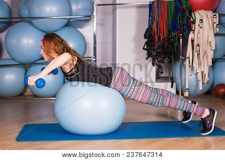 Woman Exercising With Dumbbells On A Fitness Ball.