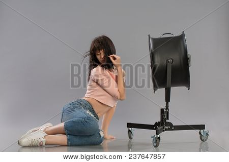 Young Sexy Female Model Posing With Working Wind Machine On Grey Background