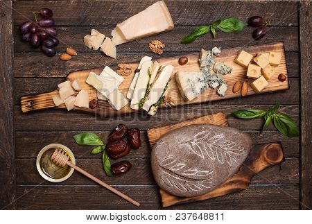 Cheese Platter With Different Cheeses, Grapes, Nuts, Honey, Bread And Dates On Rustic Wooden Backgro