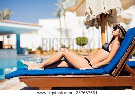 Happy Young Woman Relaxing On Sun Bed By The Pool