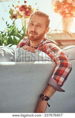 A Young Handsome Redhead Model Man Sits On A Sofa In The Room With A Loft Interior.