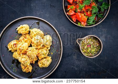 Traditional Kazakh manti steamed with mincemeat and tomato salad as top view on a modern style plate 