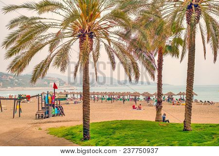Malaga, Spain - April 21, 2018. People Sunbathing On Sunbeds And Umbrellas Straw, Malagueta Beach, M