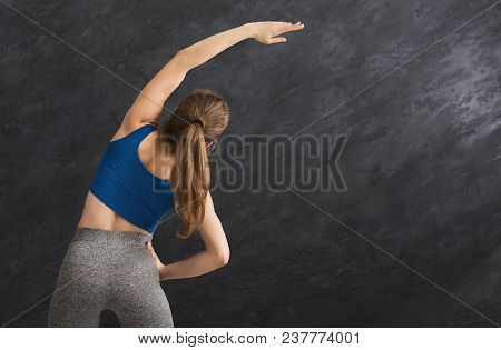 Young Woman Warming Up Before Training At Gym. Slim Girl Makes Aerobics Exercise At Gray Background 