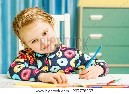 Charming blonde little girl with beauriful eyes draws with pencils and looks at camera
