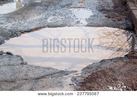 Dangerous Destroyed Roadbed. The Bad Asphalted Road With A Big Pothole Filled With Water. Mirror Ref
