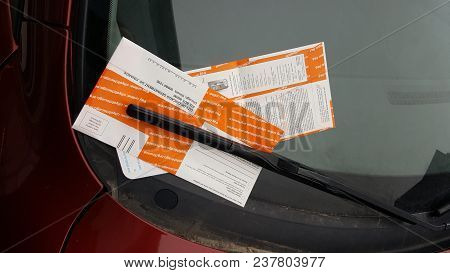 A Pair Of Two Orange And White Parking Tickets Tucked Underneath The Windshield Wiper Of A Car, Chic
