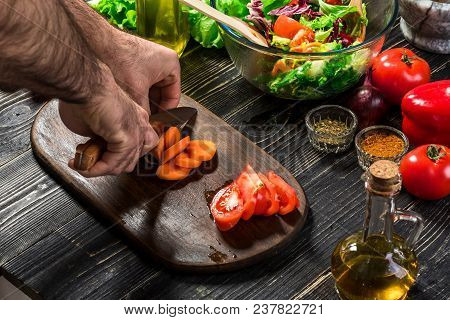 Chef Man Cooking In The Kitchen. Man's Hand Cuts Carrot On A Wooden Board