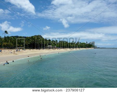 Waikiki, Hawaii - June 17, 2014:  People Play In Calm Ocean Water At Queens Beach In Waikiki With Di