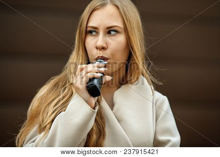 Vape Teenager. A Young Cute White Girl Is Vaping An Electronic Cigarette On The Street In Sping. Bla