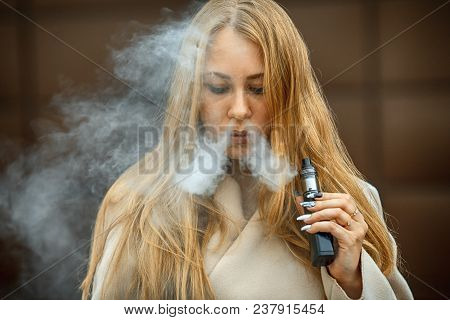 Vape Teenager. A Young Cute White Girl Is Vaping An Electronic Cigarette On The Street In Sping. Bla