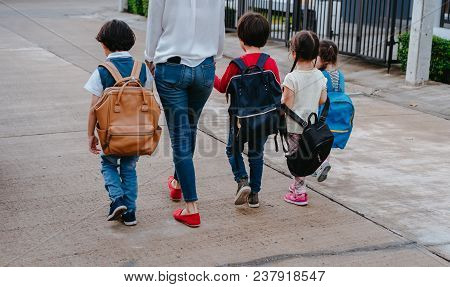 Mother And Pupil And Kids Holding Hands Going To School In First Class With Schoolbag Or Satchel Wal