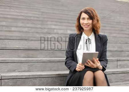 Female Secretary Sitting On Stairs With Tablet. Concept Of Working In Open Ait And Modern Technology