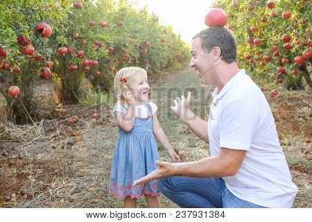 Portrait Of Happy Smiling And Laughting Father With Cute Baby Daughter Having Fun In The Pomegrate F
