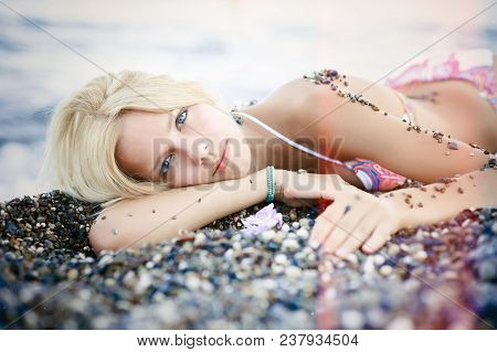 Exquisite Beautiful Blond Woman Lies On The Beach From The Pebbles Sunny. Gentle And Bright On A Sea
