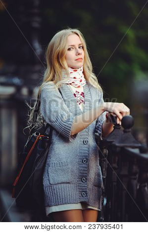 Beautiful Blond Woman Standing In The City At Night Dressed In A White Dress And A Sweater On Her Ne