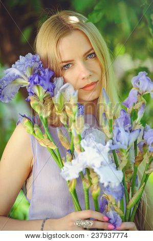 Attractive Young Girl With Blonde Dren Hair And Natural Make-up Smelling Blue Purple Iris Flowers On