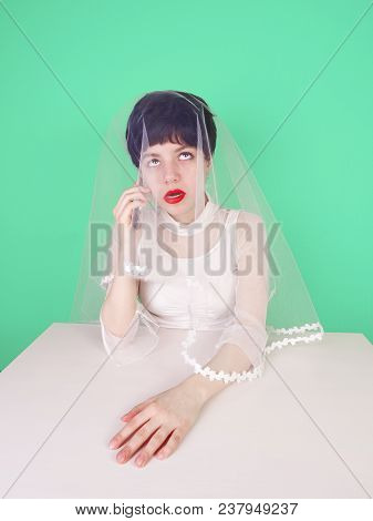 Sad And Worried Bride Talking At Mobile Phone With A Tedious Man Sitting At A Table On A Softly Turq