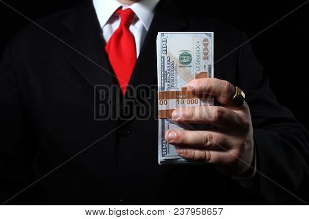 Photo of a rich businessman in black siut with red tie holding a money pack.