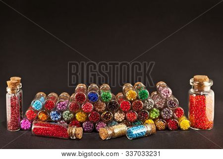 Red, Yellow, Blue, Green, Purple, Pink And Orange Beads In Glass Jars On Black Background. Beads In 