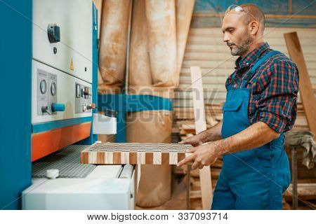 Carpenter works on woodworking machine, factory