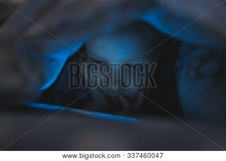 Little Girl Child Playing On Smartphone In The Evening At Home Under The Blanket When It Is Already Dark. Screen Light Reflects On Her Face