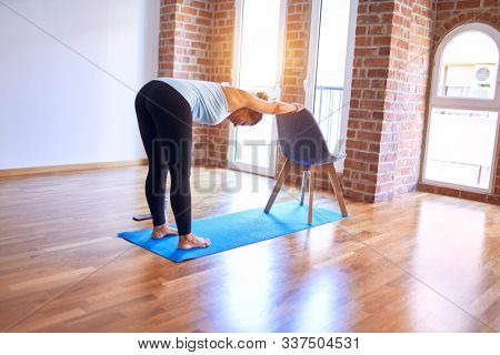 Middle age beautiful sportwoman standing on mat. Practicing yoga doing down dog on chair pose at gym