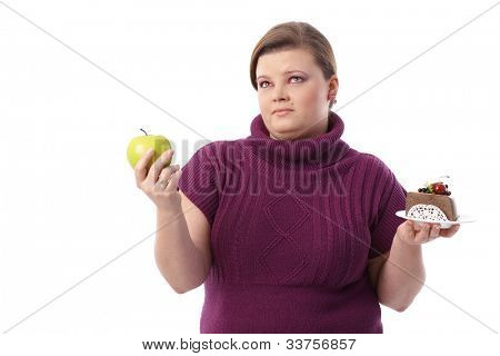 Mulher com sobrepeso hesitando entre bolo de chocolate e maçã verde.