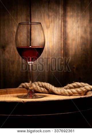 Still Life With A Glass Of Red Wine. A Glass Of Red Wine Standing On An Old Barrel Against The Backg
