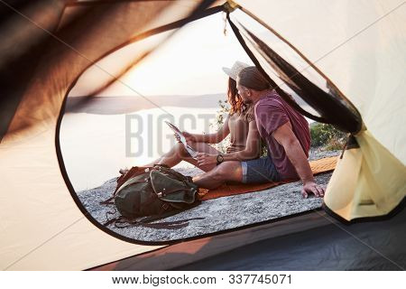 View From Tent Of Couple With Map Lying A View Of Lake During Hiking Trip. Avel Lifestyle Concept Ad