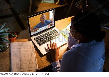 African american woman using laptop for video call, with elementary school pupil on screen. communication technology and online education, digital composite image.