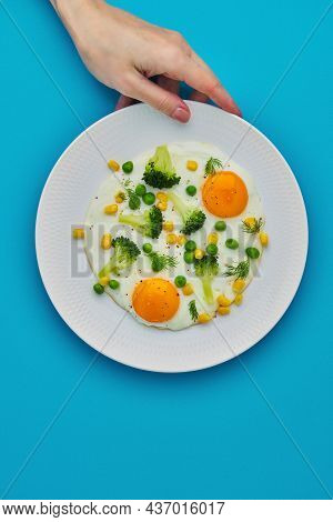 Unrecognisable Female Hand Touching Plate With Fried Eggs, Broccoli, Corn, Polka Dots On Blue Backgr