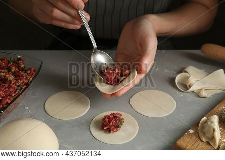 Woman Putting Gyoza Filling In Center Of Dough Wrapper At Grey Table, Closeup