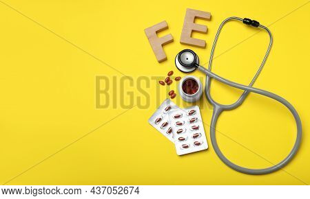 Wooden Letters Fe, Pills And Stethoscope On Yellow Background, Flat Lay With Space For Text. Anemia 