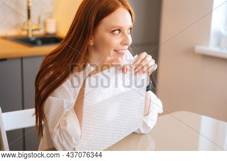 Close-up High-angle View Of Happy Young Woman Playing Pops Bubble Wrap To Calm Herself Sitting At Ta