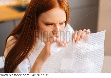Close-up Face Of Nervous Young Woman Playing Pops Bubble Wrap To Calm Herself Sitting At Table In Ki
