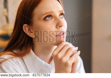Close-up Face Of Faithful Young Woman Praying Holding Folded Hands In Front Of Face At Home, Looking