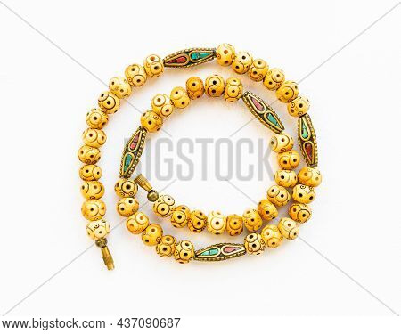 Top View Of Coiled Vintage Necklace From Carved Bone And Inlaid Brass Beads On White Paper