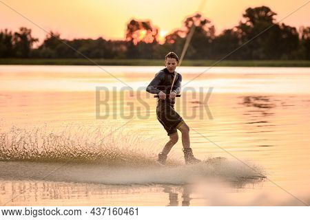 Active Man Wakesurfer Riding Splashing Wave Against Bright Sunset Background